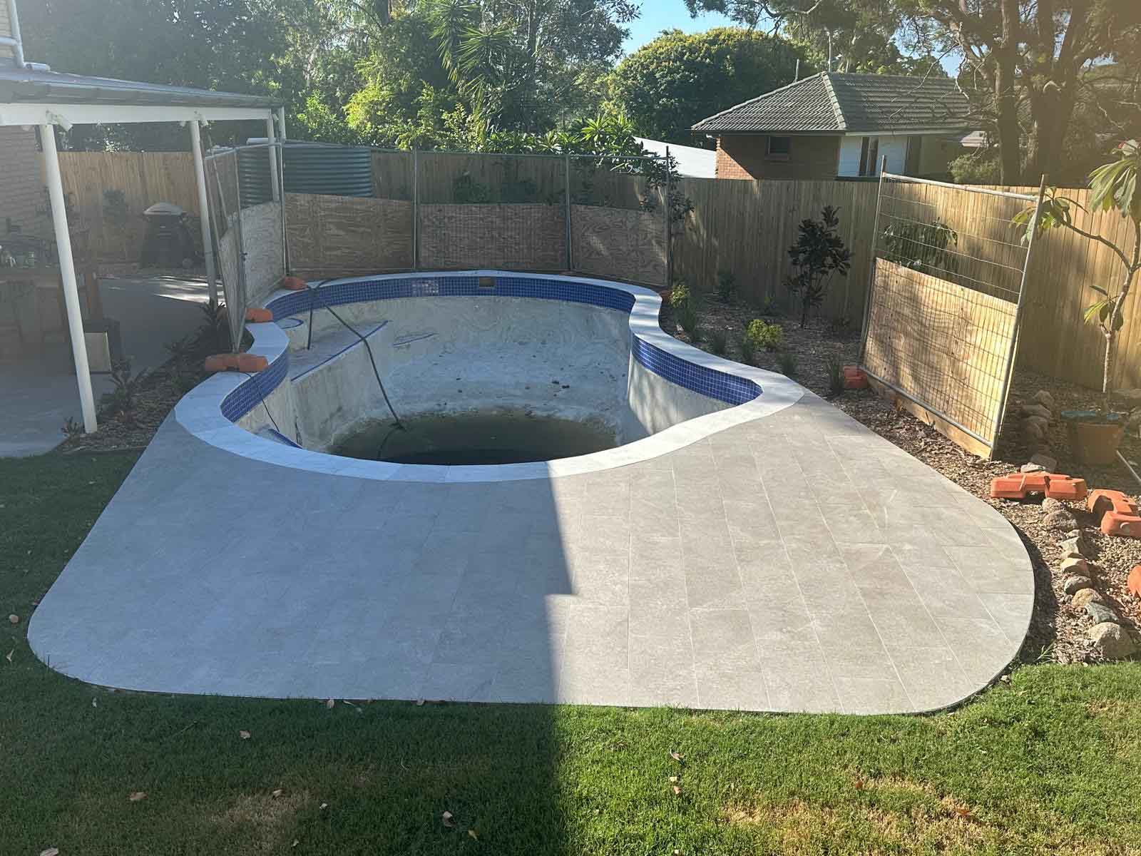 Empty kidney-shaped pool with blue waterline tiles and a pale tiled surround