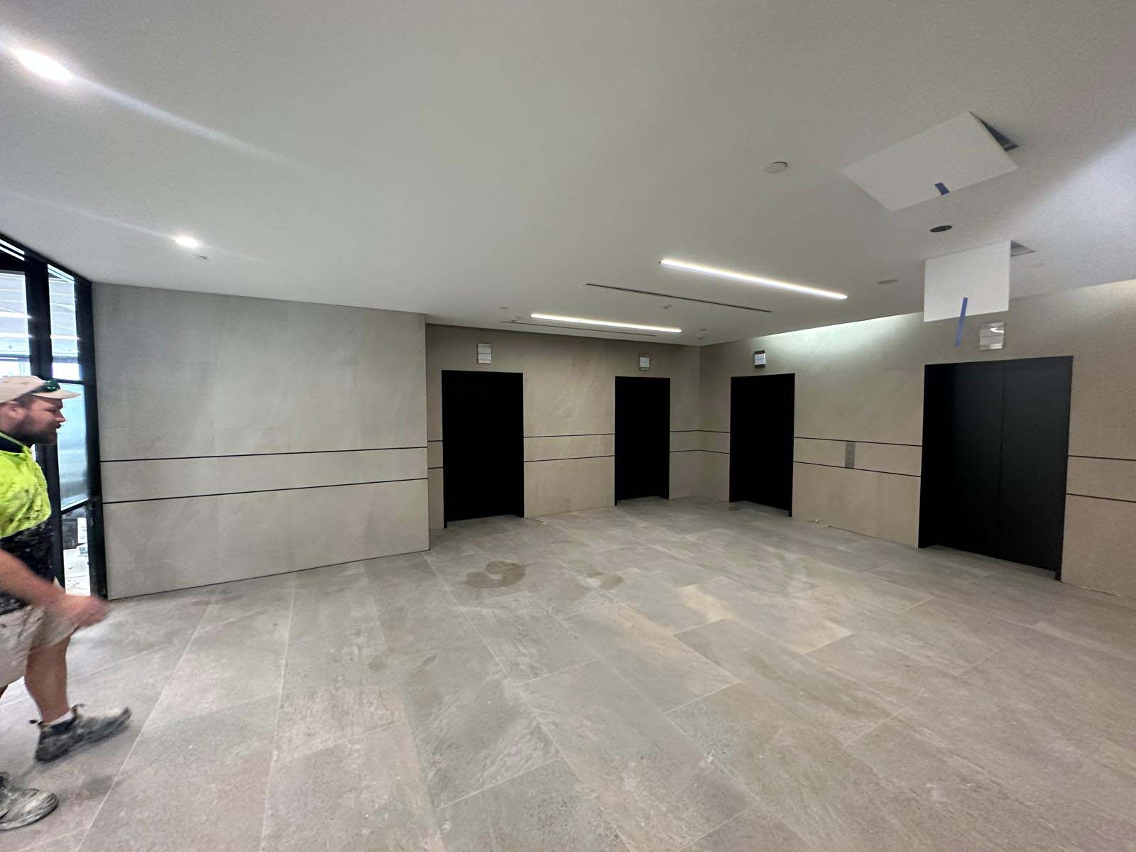 Worker in hi-vis at the edge of a foyer with grey tiled walls and black doors