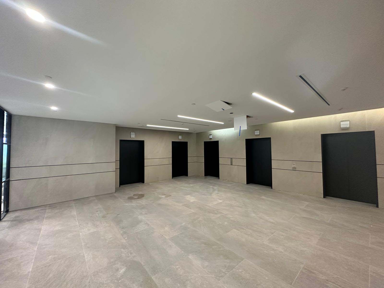 Empty foyer with large-format grey floor and wall tiles and black doors