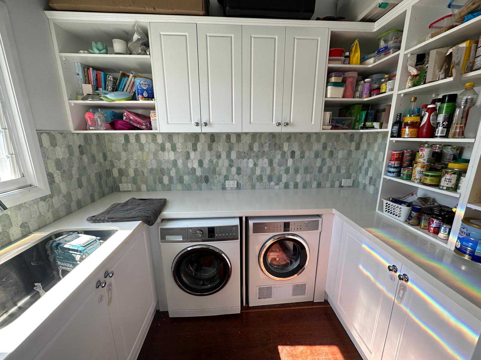 Laundry with a green hexagon mosaic splashback above a washer and dryer