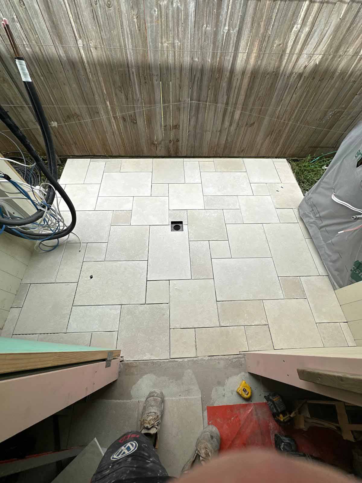 Small courtyard tiled in cream mixed-size pavers around a drain