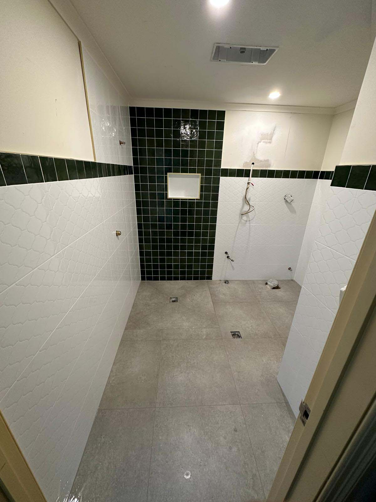 Bathroom with a dark green tiled shower wall, white wall tiles and grey floor