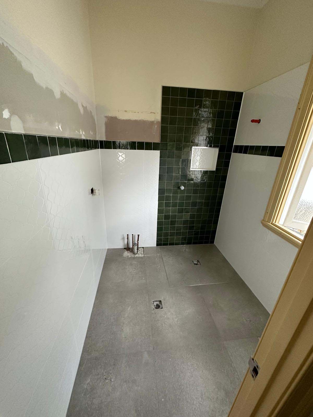 Dark green tiled shower wall and white wall tiles beside a window, before fit-out