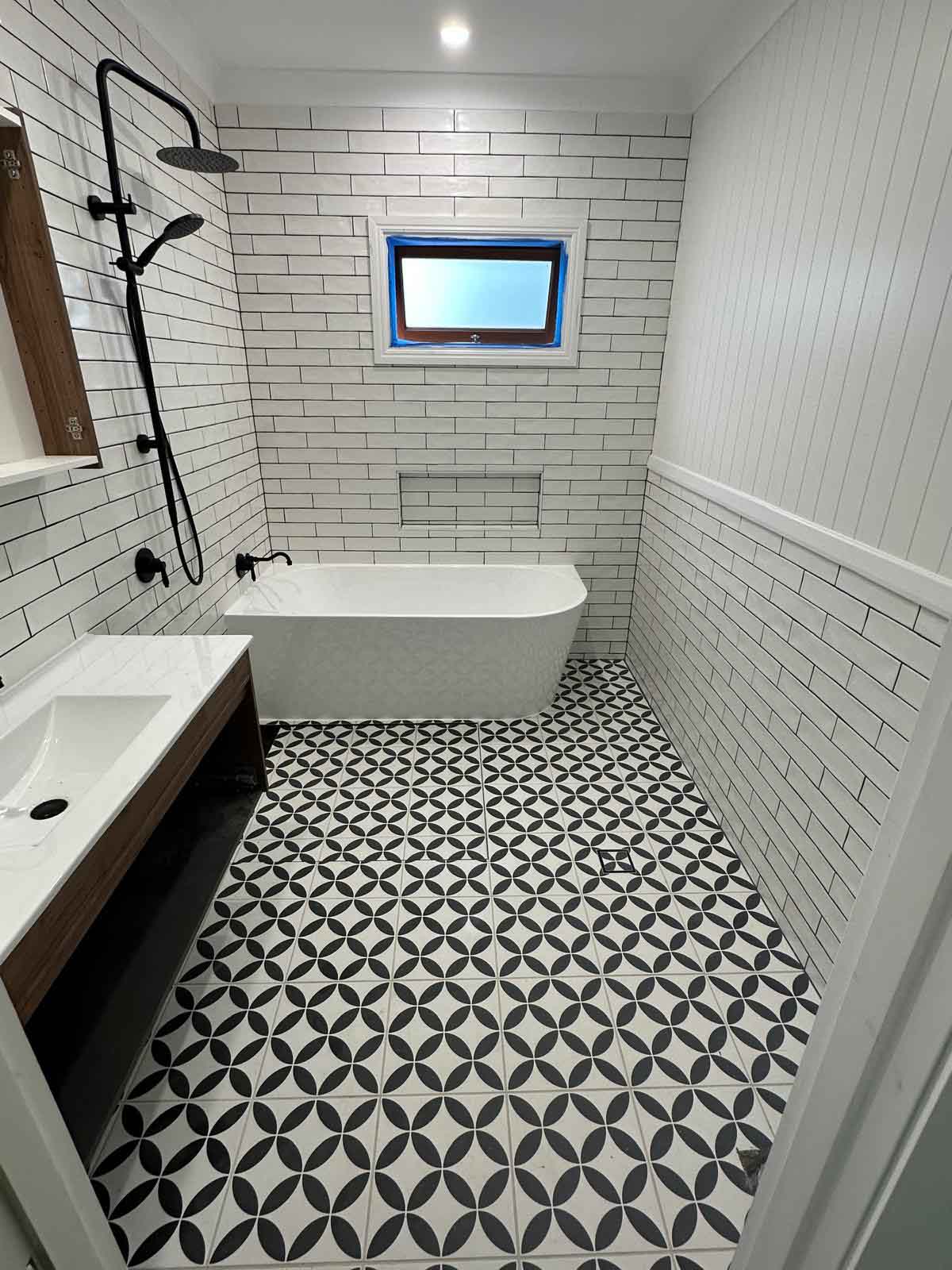 Finished bathroom with black and white patterned floor, freestanding bath and subway tiles