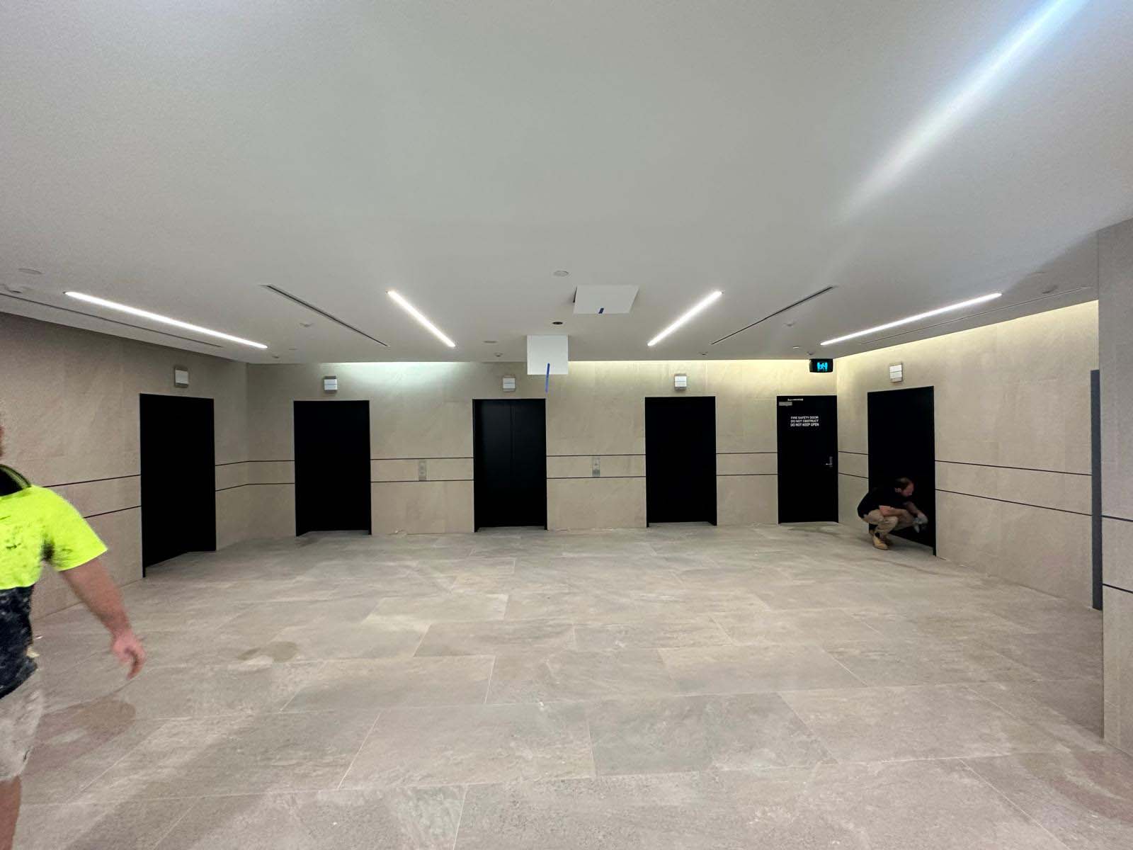 Worker in hi-vis walking through a foyer with large-format grey floor and wall tiles