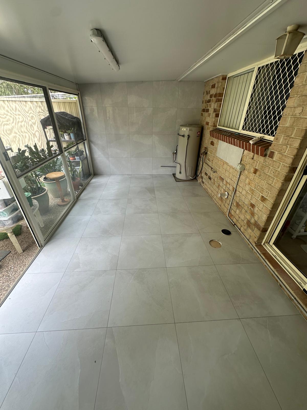 Enclosed patio with large light grey floor tiles beside a brick wall