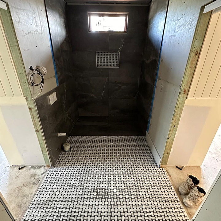 Bathroom mid-renovation with dark stone-look wall tiles and a black and white mosaic floor