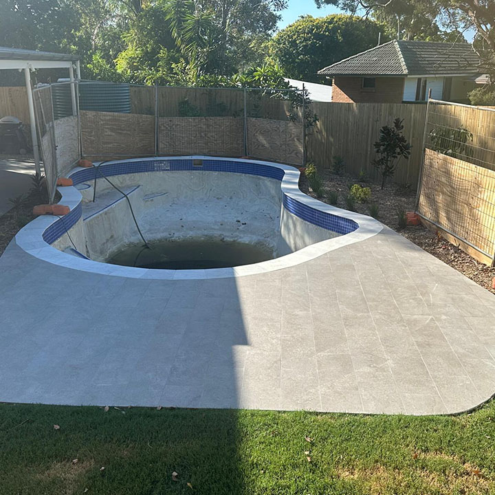 Kidney-shaped pool with blue waterline tiles and a pale tiled surround